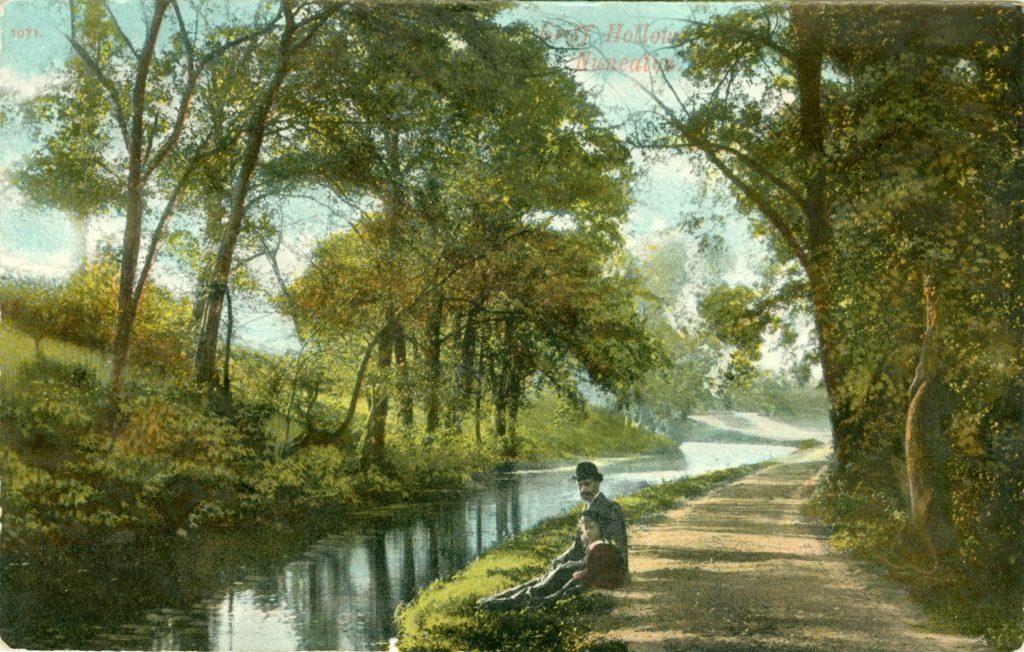 A colour postcard showing a canal lined with trees. A man and a child are sitting along the side of the water.