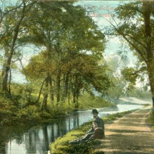 A colour postcard showing a canal lined with trees. A man and a child are sitting along the side of the water.