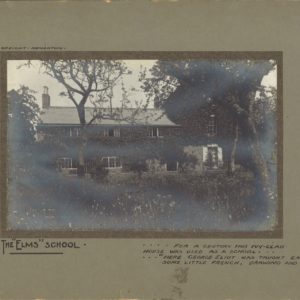 Black and white photograph showing a house whose wall are clad in ivy. Trees and bushes are all around the front of the building. Image is within a green/brown card mount. The words The Elms School are written on the mount.