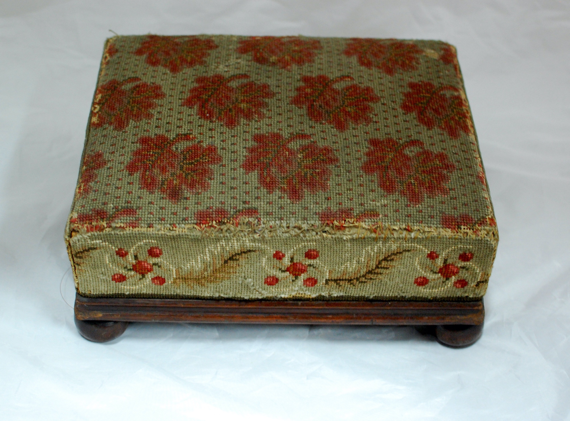 Wooden footstool with embroidered cushion. It is embroidered with a red flower pattern.