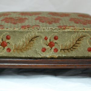 Side view of a wooden footstool with embroidered cushion. It is embroidered with a red flower pattern.