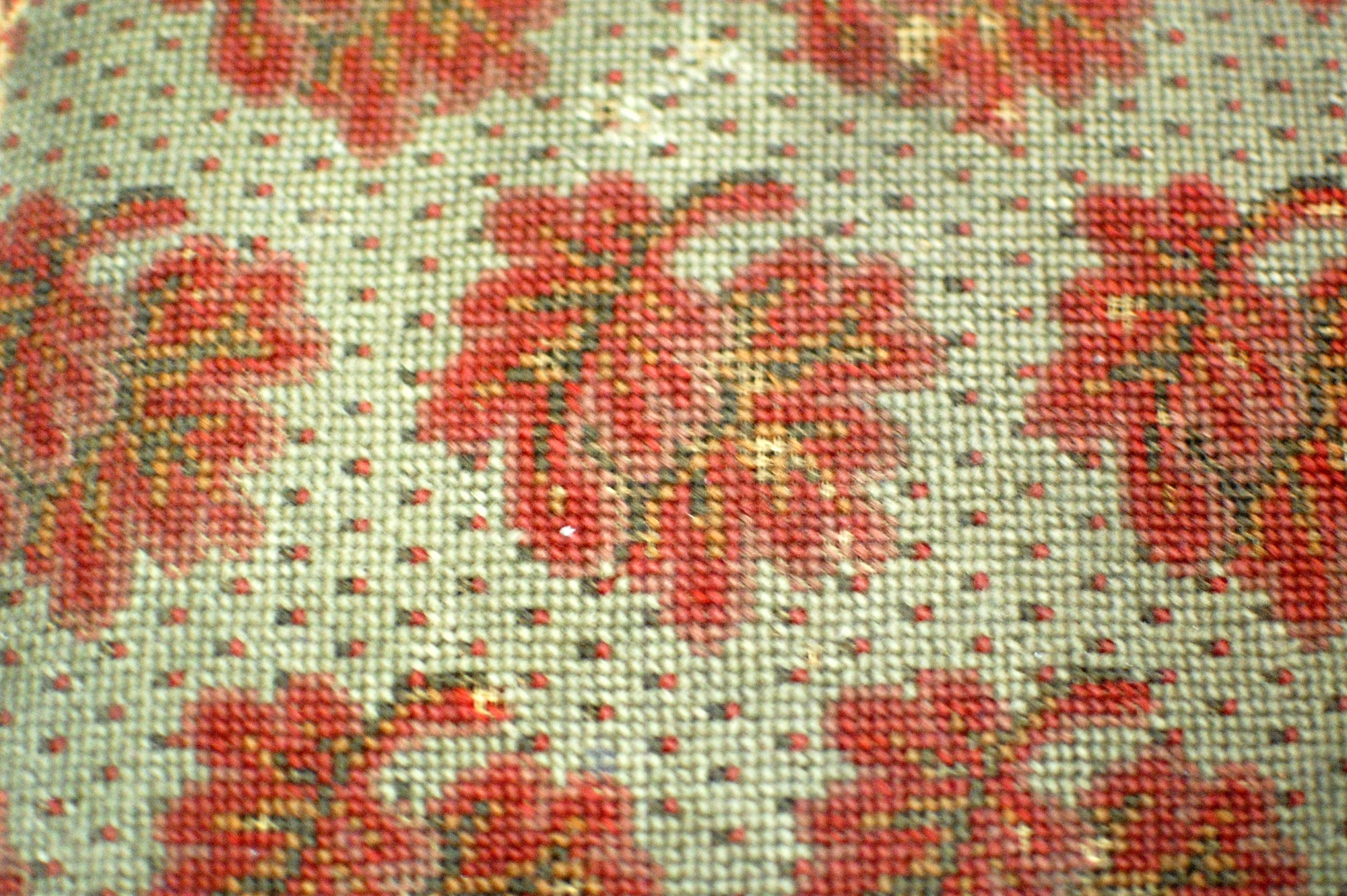 Detail of the top of a footstool. Detail shows embroidered red flower pattern.