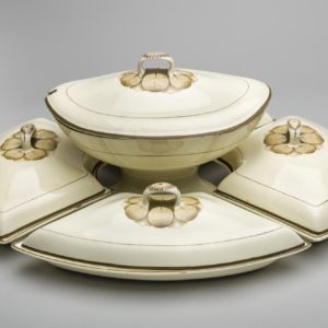 A supper set made up of one cream coloured boat shaped tureen on a stand and four dishes. All have lids decorated with a brown central circular leaf design and flowers on the handles.