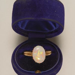 Open blue ring box. Inside is a gold ring set with a large opal stone.