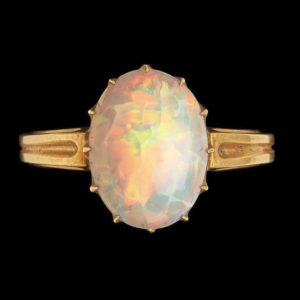 Large gold ring set with a large opal. Photographed on a black background.