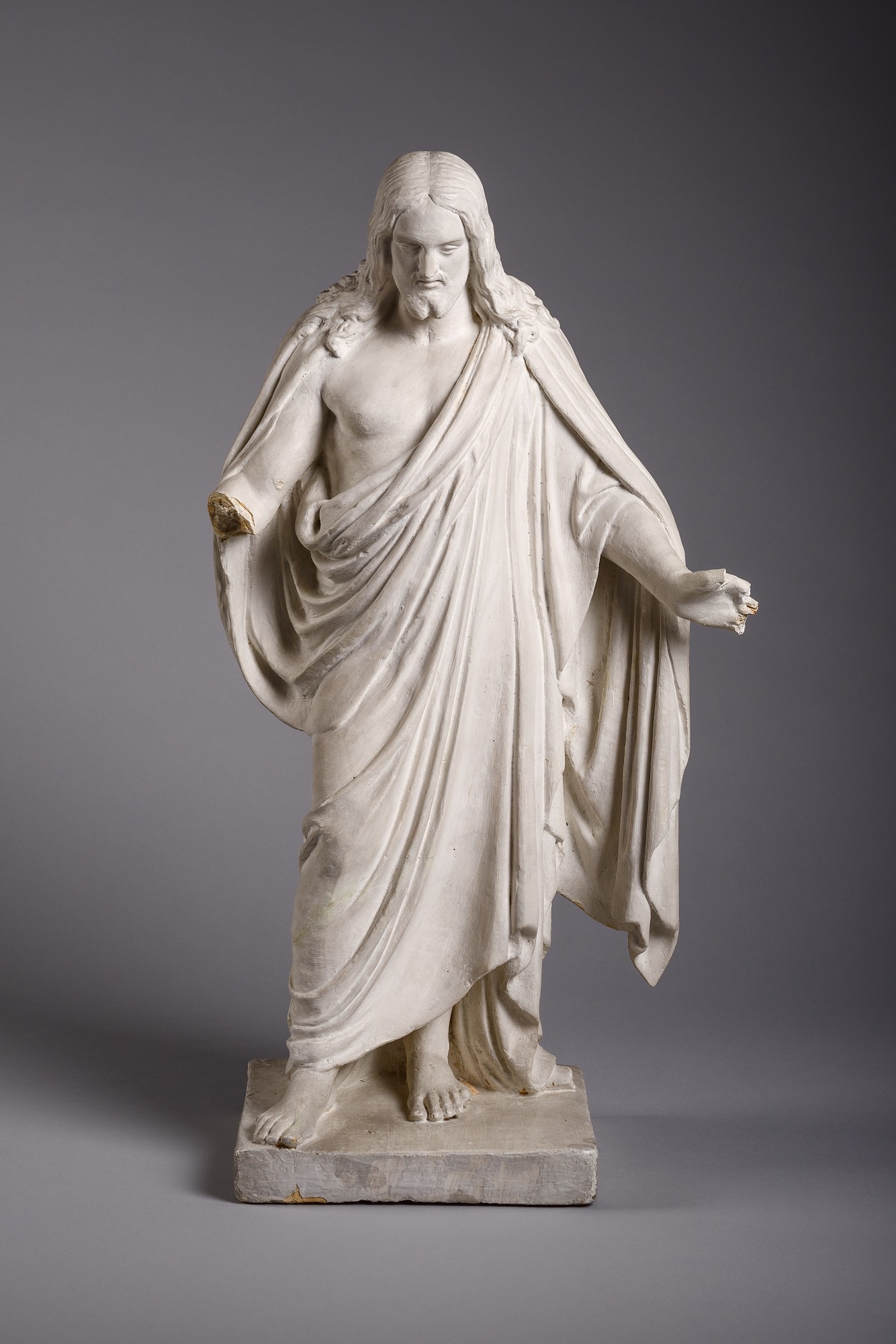 A small statue of a figure with long hair and arms slightly outstretched. The figure is wearing robes.