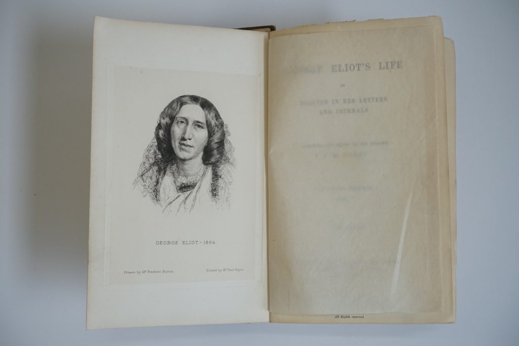 Pages from an open book. The left hand side shows a portrait of George Eliot. The right hand side page is obscured by an inner cover. It reads George Eliot's Life as related in her letters and journals. Arranged and edited by her husband J.W Cross in three volumes.