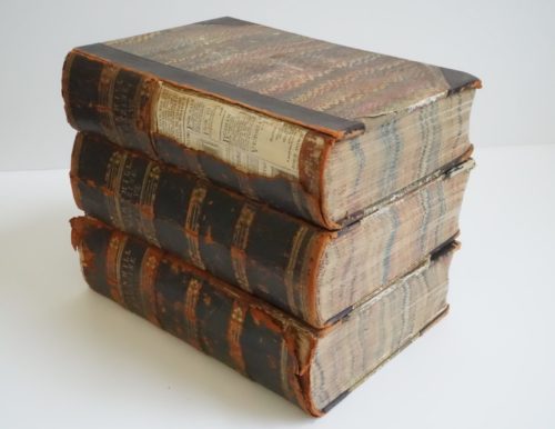 A stack of three books. There is damage to the spine of the top book revealing newspaper underneath. Cornhill Magazine is typed in gold on the spine of each book.