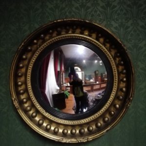 Circular mirror in ornate frame decorated with large spheres and leaves at the bottom, top and each side.