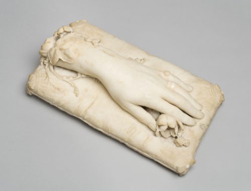 White marble sculpture of a hand and part of arm mounted on a rectangle marble cushion. Under the hand is a sculpted marble rose.